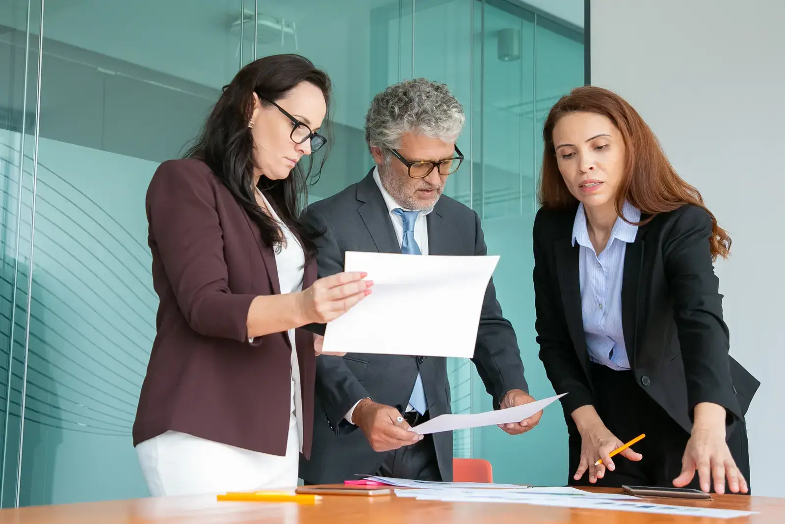 Three colleagues standing at a table reviewing printed documents together
